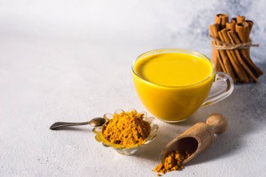 Beyaz zemin üzerinde altın zerdeçal sütü ve baharatlı tarçın ve malzemeler.