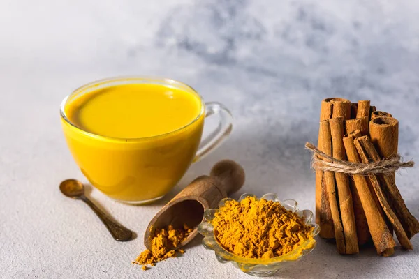 Beyaz zemin üzerinde altın zerdeçal sütü ve baharatlı tarçın ve malzemeler.
