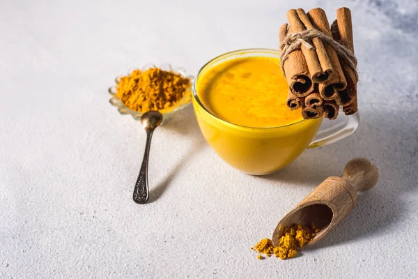Beyaz zemin üzerinde altın zerdeçal sütü ve baharatlı tarçın ve malzemeler.