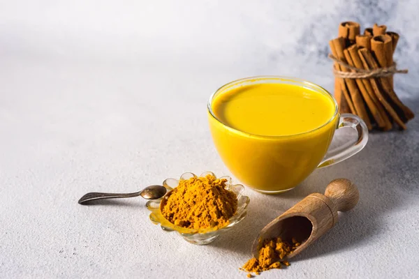 Beyaz zemin üzerinde altın zerdeçal sütü ve baharatlı tarçın ve malzemeler.