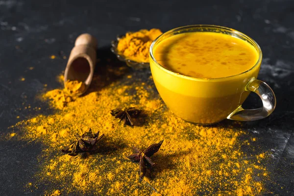 Koyu arkaplanda tarçın ve malzemelerle birlikte altın zerdeçal sütü.