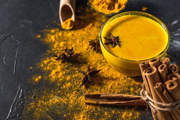 Koyu arkaplanda tarçın ve malzemelerle birlikte altın zerdeçal sütü.