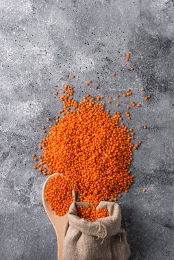 Gri arka planda mercimek ahşap kaşıkta kırmızı mercimek ve yakın plan sağlıklı yiyecek.