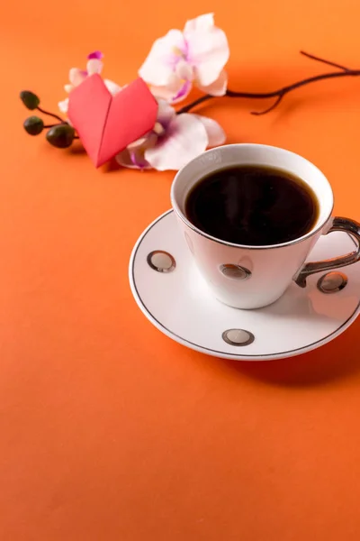 cup of aromatic coffee and an orchid branch on an orange trendy background with space for text
