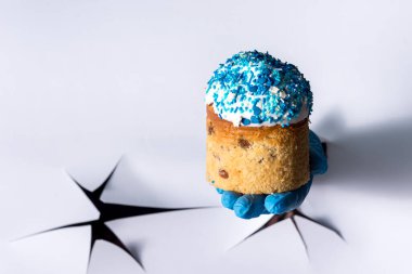 Kağıt duvardaki bir delikten, mavi tıbbi eldivenli bir kadın eli Paskalya pastası tutuyor.