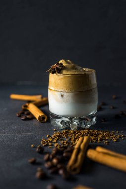 Dalgona kahvesi şeffaf bir fincanda, koyu bir arka planda. Kremalı kahve, şeker ve sütlü Güney Kore içeceği..