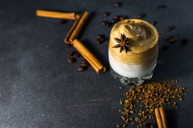 Dalgona kahvesi şeffaf bir fincanda, koyu bir arka planda. Kremalı kahve, şeker ve sütlü Güney Kore içeceği..