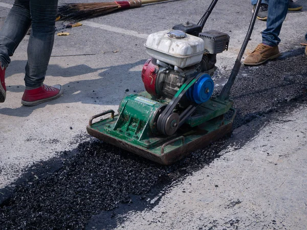 Trabajador utiliza compactador de placa vibratoria compactando asfalto en carretera — Foto de Stock
