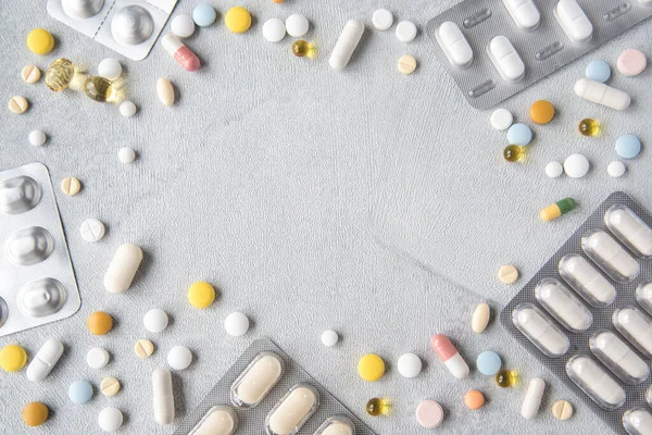 Frame of drugs and pills on a light background. Multi-colored pills, capsules, vitamins laid out in the form of gray on a blue background. Shot from the top. Concept of Health Care. Copy space.