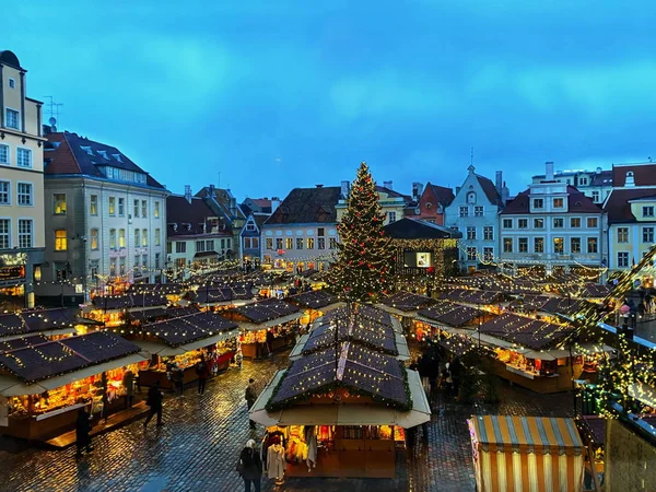 night  Christmas  tree from restaurant window view on Old town hall square holiday in Tallinn medieval street  city. tree  people walking under umbrellas on street  blurred evening light lamp life style  urban travel to Estonia in Europa 