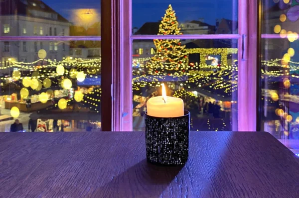 Christmas holiday in Europe  Christmas marketplace  tree light decoration  new year  old town square  light market place Estonia from restaurant window and candle light on table  festive background Candle light blurred illumination