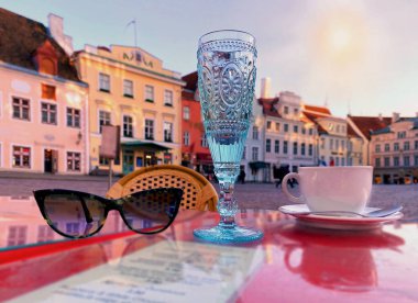 Mavi bardak şarap, beyaz bardak kahve ve güneş gözlüğü kırmızı masanın üstünde sokak kafeteryasında, mavi gökyüzü, ortaçağda güneşli bir gün, günbatımının yansıması evlerin Tallinn 'e seyahati, Estonya