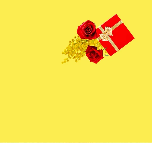 red roses and  box for gift with  gold bow flowers  branch mimosa on  yellow background template for greetings card Women day , Valentine day , copy space