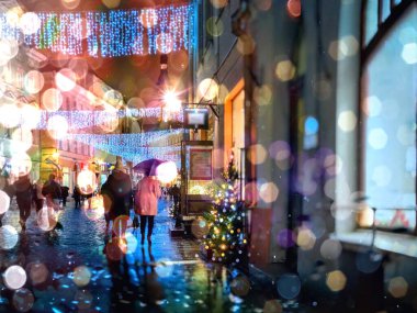 Şehir gecesi Tallinn Noel 'inde hafif yağmurlu geçti. Eski kasaba sokaklarında insanlar şemsiyelerle yürüyor. Yağmur damlaları yaşam tarzlarını yansıtıyor. 