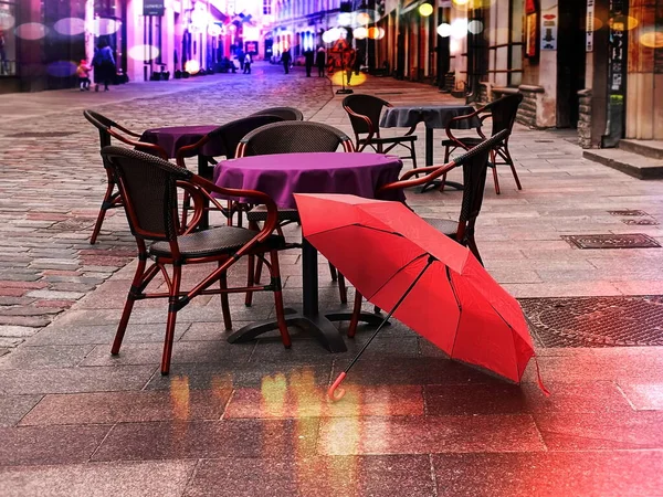 Rainy evening in city street cafe tables empty pink umbrella on old pavement people walking store blurred light Tallinn old town Estonia