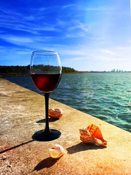 beach restaurant ,summer seaside leisure  glass of red wine on stone and seashells nature panorama blue sky and sea water  reflection romantic  cafe background