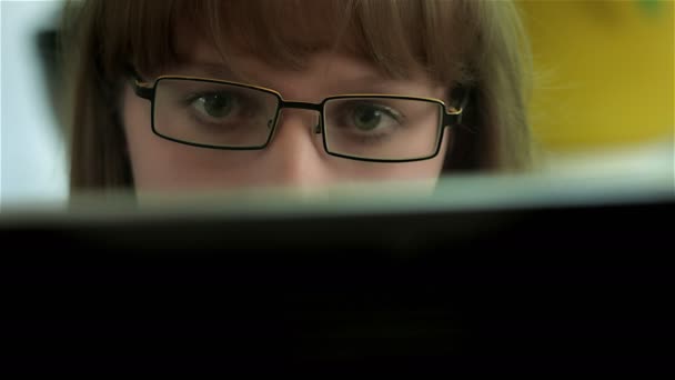 Дівчина з окулярами здивована чимось, побаченим на моніторі комп'ютера — стокове відео
