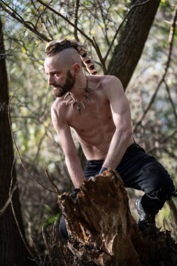 Genç bir adam ağaçta oturuyor, saçında kemik mücevherleri var..