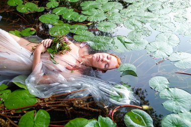 Genç, seksi, mutsuz, deli kadın Ophelia. Kıvırcık kızıl saçlı, çiçekli, gözleri kapalı gölde ölüyor.