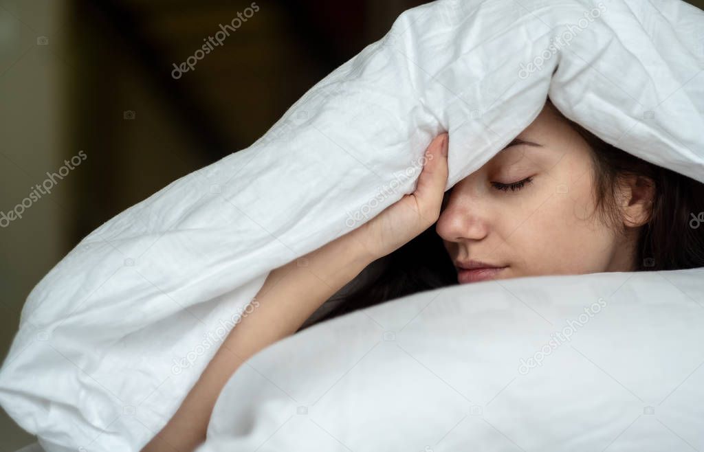 Portrait of an attractive, young, sexy dark haired woman in Bed, hand and head on the pillow under the blanket, Copy space.