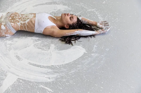 La tête et le torse d'une jeune femme sexy avec les mains tendues, peintes artistiquement avec de la peinture blanche, se trouve sur le sol dans un atelier d'artistes . — Photo