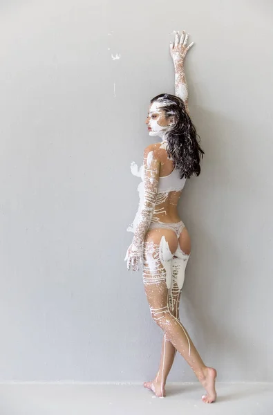 Jeune femme peinte artistiquement abstraite en sous-vêtements, vêtements de sport, avec du blanc, peinture, rouleaux devant le mur en studio et laisse des impressions couleur, espace de copie . — Photo