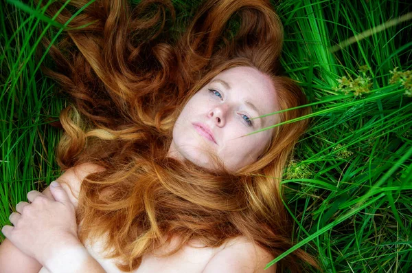 Retrato de una hermosa mujer de pelo rojo sexy, tumbada al sol en la felicidad, relajándose en la hierba verde, el pelo rojo cubierto libremente alrededor de la cabeza . —  Fotos de Stock