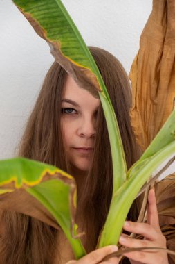 Genç, şişman, şişman, kahverengi saçlı bir kadının portresi. Yeşil ve kuru, kurumuş dekoratif muz ağacı yaprakları, kesilmiş, beyaz arka plan, uzay kopyası.