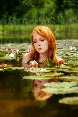 Narin, genç, seksi, kızıl saçlı kadın, pembe bir su çiçeğinin üzerinde şehvetli, şehvetli, şehvetli bir şekilde, göl, göl ve gölden zevk alır..