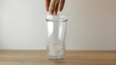 Buz küplerini boş bardağa atan bir kadın. Arka planda açık tahta bir zeminde. Buzlu kahve yapıyor..