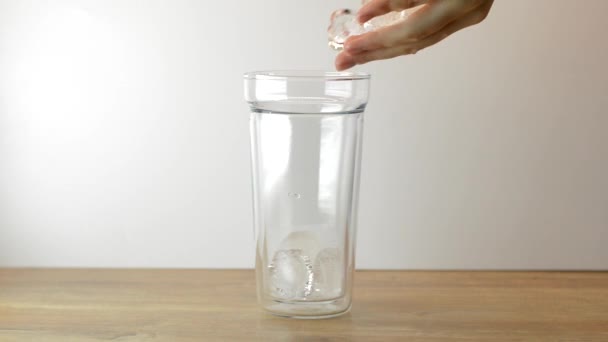 Femme jetant des glaçons dans du verre vide sur un fond en bois clair. .