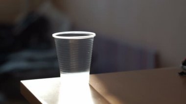 Mans plastik şişeden plastik bardağa maden suyu döker, sonra onu içer ve bardağı masanın üzerine koyar.