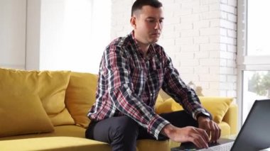 Rahat bir odada kanepede oturan kendine güvenen ve odaklanmış serbest çalışan bir genç. Başarılı, düşünceli, bin yıllık bir adam akıllı evdeki dizüstü bilgisayarda çalışıyor.