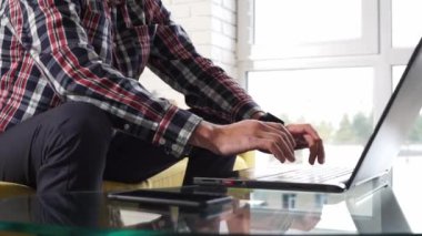 Klavyede yazı yazan ellerin yakın çekimi. Rahat bir odada kanepede oturan serbest çalışan genç bir öğrenci. Başarılı, düşünceli, bin yıllık bir adam dizüstü bilgisayarda çalışıyor, cam masada elinde akıllı bir telefon tutuyor.