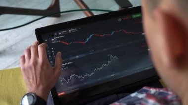 Genç serbest çalışan rahat bir odada kanepede oturuyor ve bilgisayarın dokunmatik ekranındaki kripto para şemasını kontrol ediyor. Pazarlık yapan başarılı bir tüccar. Bitcoin ticareti, engelleme zinciri, sanal para