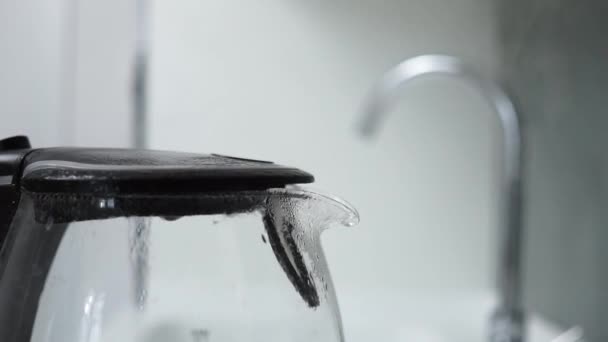 Primer plano de la olla de té de agua caliente eléctrica transparente de vidrio en una moderna cocina blanca de alta tecnología en un apartamento loft casa inteligente. El agua se hierve para hacer té o café. El vapor viene de la tetera. — Vídeos de Stock