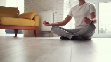 Genç modern Kafkasyalı adam pencerenin önünde oturmuş yoga nilüfer pozu çalışıyor. Adam evde meditasyon yapıyor. Yatıştırma ve yatıştırmanın tadını çıkarıyor. Uyum saglik yasam tarzi.