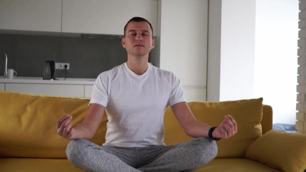 Young modern caucasian man practice yoga lotus pose sitting on a yellow couch. Man meditating at home enjoying appeasement and pacification. Harmony wellness lifestyle. Youth and meditation concept. — Stock Video