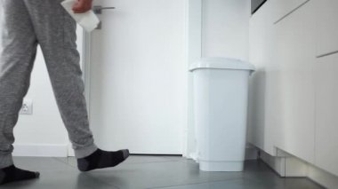 Tanınmayan bir adam beyaz bir çöp kutusuna doğru yürür ve evinde bir kağıt havlu atar. Akıllı bir evde parlak bir mutfak.