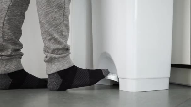 Unrecognizable man walks up to a white bin and throws out a paper towel at home. Bright kitchen in a smart home — Stock Video