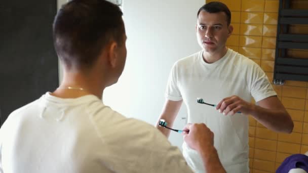 Young Man Brushing Teeth In Bathroom in front of mirror. Doing hygiene routine looking in mirror. Dental oral care at morning. — Stock Video