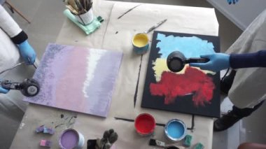 Artists dry abstract paintings with hair dryers. Art Studio. Paint cans and brushes. Top view