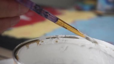 Male hand dips his brush in the paint can. Colored background. Art Studio. Collaboration.