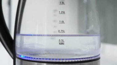 Close-up of glass transparent Electric Hot Water Tea Kettle Pot in a modern white high-tech kitchen in a smart home loft apartment. Water is boiled to make tea or coffee
