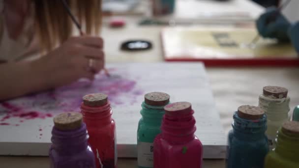 Multicolored bottles of paint. Girl artist draws letters on the color board. — Stok video