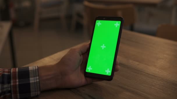 Close-up de um Mans mão segurando verde Mock-up Screen Smartphone. Usando o aplicativo. Telefone móvel moderno. No fundo aconchegante Sala de estar ou Home Office . — Vídeo de Stock