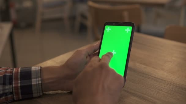 Zbliżenie Mans Hand Holding Green Mock-up Screen Smartphone. Używanie aplikacji. Nowoczesny telefon komórkowy. W tle przytulny salon lub Ministerstwo Spraw Wewnętrznych. — Wideo stockowe