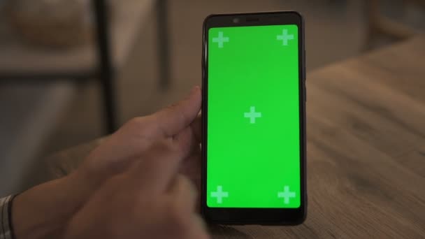 Zbliżenie Mans Hand Holding Green Mock-up Screen Smartphone. Używanie aplikacji. Nowoczesny telefon komórkowy. W tle przytulny salon lub Ministerstwo Spraw Wewnętrznych. — Wideo stockowe