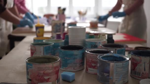 Paint cans in the foreground. People in aprons draw — Stockvideo