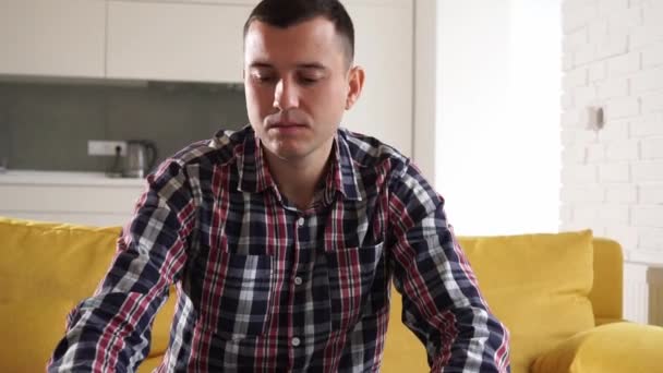 Serious confident and focused young man freelancer student sitting on the sofa in cozy room. Successful thoughtful millennial guy works at a laptop, holds a smartphone in his hand — Stock Video